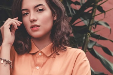 woman in orange collared shirt with a plant behind her