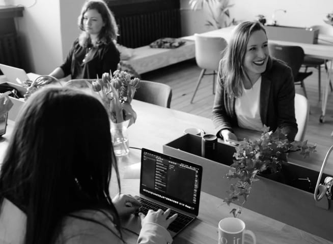 three employees sitting at a desk working on their laptops